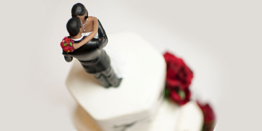 a white wedding cake with red flowers and a cake topper bride and groom dancing on top